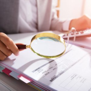 Business woman analyzing invoice with magnifying glass