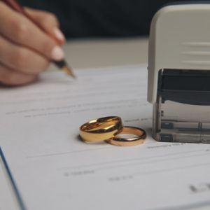 Hands signing letter of divorce with 2 ring