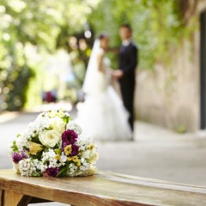 Bouquet on wooden bench with bride and groom