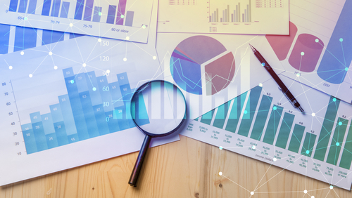 Magnifying glass and documents with analytics data lying on table 