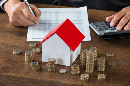 Stacks of coins, house miniature, and a man writing with calculator