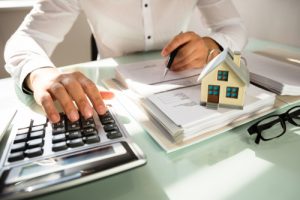 Businessman’s Hand Calculating Invoice With House Model In Office