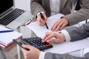 Two Female Accountants Counting On Calculator Income For Tax Form