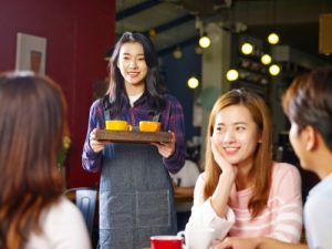 Young Smiling Asian Waitress Serving Customers In Coffee Shop  Focus