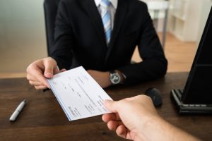 Close-up Of Businessman Hands Giving Cheque To Other Person