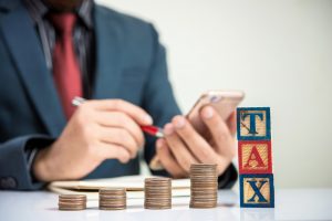 Businessman,And,Stack,Of,Coins,With,Tax,Word,,Money,Saving