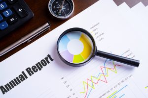 Magnifying glass on colourful pie chart with “Annual Report” text on paper.